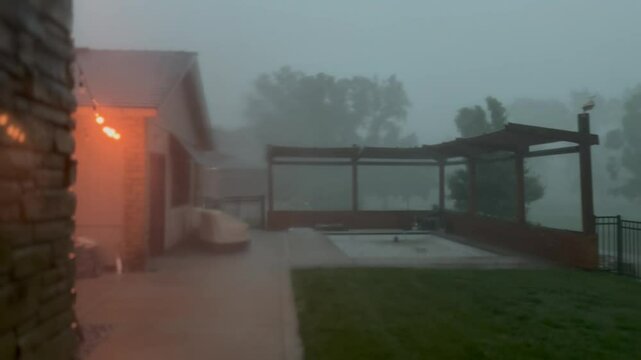 A storm with Heavy rains and lighting - severe weather in and high winds hit a backyard with a pool and a pergola