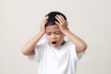 Frustrated little asian boy suffers from headache, keeps hands on temples, isolated on white background.