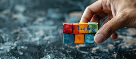 Hand holding colorful block with text "Loading" on grey background. Loading screen concept for web design and mobile app development.