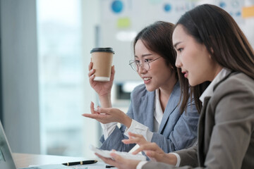Obraz premium Two women are sitting at a desk, one holding a cup of coffee