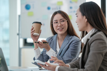 Two women are sitting at a desk, one holding a cup of coffee