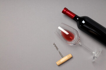 A bottle of wine, a glass and a corkscrew, on a gray background.