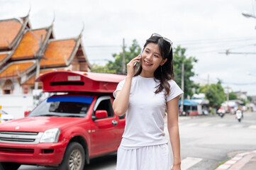 A beautiful Asian woman is talking on the phone while standing by the street in the city.