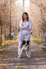 Fototapeta premium Caucasian woman walking with a dog in the park in autumn. The Border Collie jumps very high.