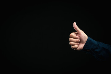 Hand showing thumbs up gesture, positive approval sign against dark background.
