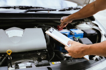 A technician in a Thailand auto repair shop conducts diagnostics on a car engine using a laptop. The scene highlights advanced technology in automotive inspection and repair.