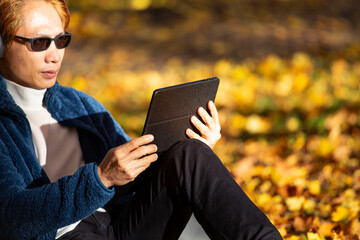 Nomad digital young asian man  with laptop and running remotely at park during a golden autumn amazing 