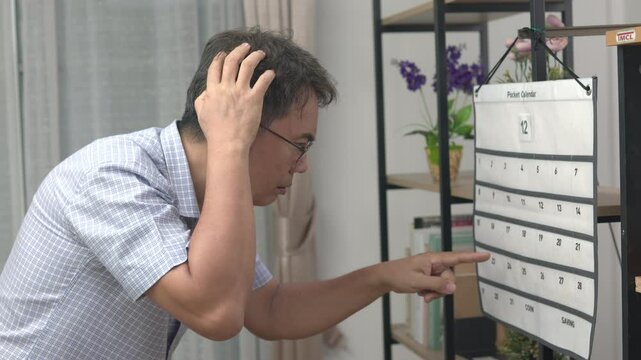 Confused Asian Senior Man With Dementia Looking At Wall Calendar.