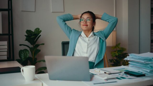 Asian accountant woman in her office is ending her work day. She stands up from her desk and relaxes after a hard day's work