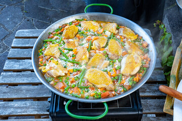 Spanish national dish Paella. Here in the variation: rice with chicken, beans, carrots and peas. The pan is on a gas cooker in the garden