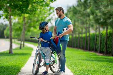 Obraz premium Father helping son get ready for school. Father and son cycling on bike on summer day. Father support child. Fathers love. Sporty kids. Cute boy with dad cycling in summer park outdoor.