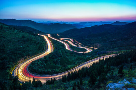 At night, on the winding mountain road, the car lights form a long stream of light