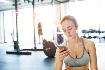 Young fitness girl checking her performance on smatphone after hard workout in gym.