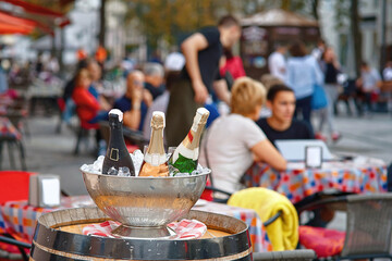 Сhampagne bottles in an ice bowl on wine barrel, creating an elegant atmosphere for restaurant guests. Summer evening at restaurant street terrace. Chilled champagne iin ice bucket