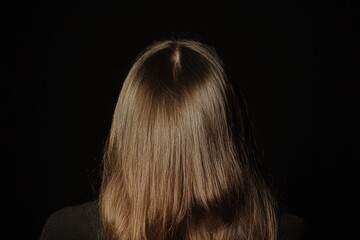 Fototapeta premium Back View of Woman with Long Brown Hair on Solid Black Background Highlighted in Middle