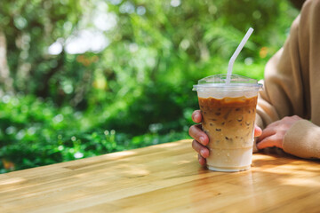A woman holding a glass of iced latte coffee on wooden table in the garden