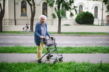 Beautiful elderly woman walking on city street with rollator, going shopping to the store.