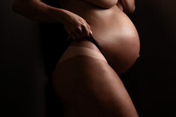 Pregnant woman pulls back her panties showing instant tan. Vertical photo. 