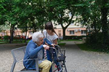 Girl helping gradma with walker to stand up from bench.