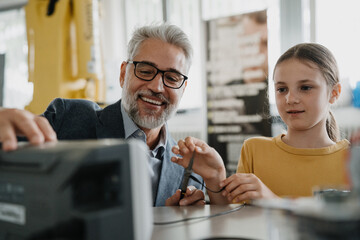 Father and girl during kid at work day, encouraging girl in career in robotics. Teacher showing young schoolgirl how to assemble small robot.
