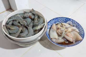 A raw squids and shrimps in bowls on a kitchen table
