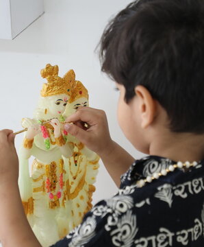 cute little indian boy is giving flute to lord Krishna and praying radhe krishna. he has wore Kurta with Radha name written in Hindi. he has devoted himseff in krishna bhakti 