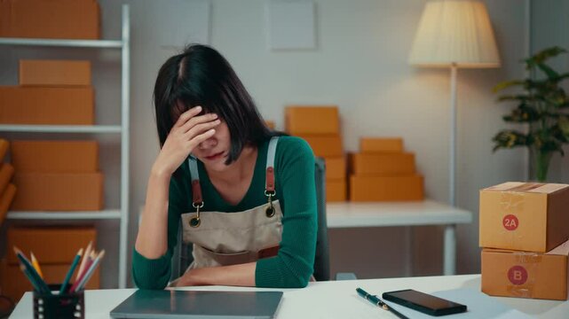 Entrepreneur is experiencing frustration while managing her online business. She is surrounded by cardboard boxes, hinting at the challenges of order fulfillment and customer satisfaction