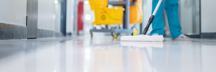 A cleaner in uniform efficiently mops the epoxy floor in the patient room, ensuring the hall floor is free from any dirt or germs.