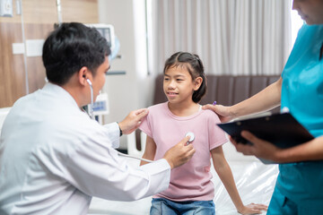 Obraz premium Asian male doctor and a female nurse gently examine a young girl in the hospital, ensuring her comfort and care throughout the process.