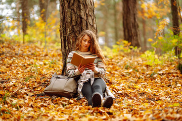 A young woman enjoys a quiet moment, immersed in a book while seated on colorful fallen leaves. ....