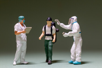 A miniature scene depicts a traveler being screened by healthcare workers. The image highlights health and safety protocols during travel in a pandemic