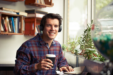 Man, portrait and notebook with headphones in coffee shop for remote work, pride or tea in morning. Person, journalist or writer with book, drink and music subscription with smile for article in cafe