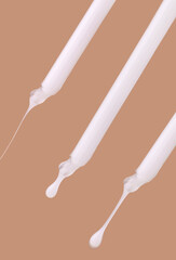 pipettes with white serum close-up falling drops on a beige background
