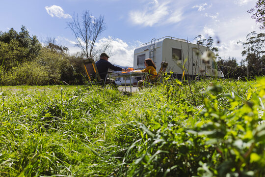 Senior couple sitting on camping chairs near motor home