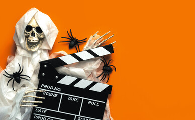 Scary evil skeleton smiling with movie clapperboard and spiders with copy space for text. Halloween...