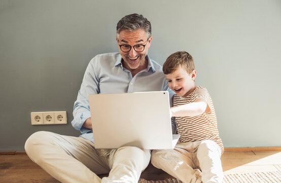 Happy grandfather using laptop by grandson at home