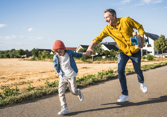 Cheerful man and boy holding hands and running on road