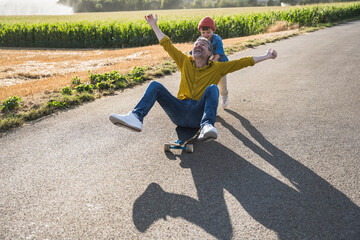Cheerful man enjoying skateboarding and grandson pushing him from behind