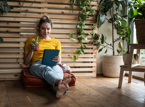 Young freelancer holding lemonade and using tablet PC sitting at home office