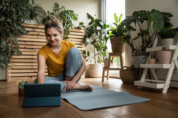 Smiling woman using tablet PC sitting on exercise mat at home
