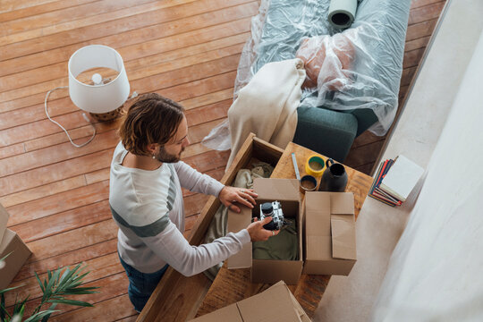 Young man packing camera in cardboard box at home