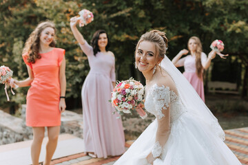 A bride and her bridesmaids pose for a picture. The bride is wearing a white dress and a veil. The...
