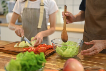 Young couple wearing aprons preparing healthy vegan salad in the kitchen