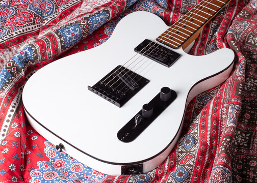 Samara, Russia - October 8, 2023: Squier Telecaster on red blanket with patterns. White guitar body on colored textile background. White electric guitar with black hardware.