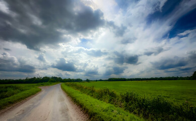An incredibly picturesque winding road that is beautifully surrounded by lush, vibrant green fields and dramatic clouds