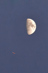 Airplane flying near half moon in clear sky