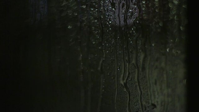 The lights of the night city. Misted glass. Liquid raindrops on the window. Defocused auto traffic lights at sunset day. Sadness and sad mood background.