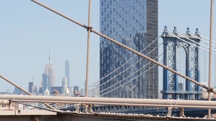 New York City Manhattan Bridge from Brooklyn Bridge view. Empire State building in Midtown. USA travel landmark, NYC skyline cityscape. Iconic architecture thru cables. Visit United States of America.