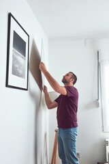 Man hanging pictures on the wall, cleaning and remodeling apartment.