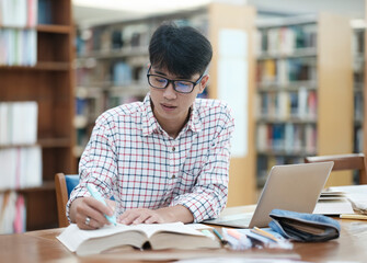 Young Asian male sitting inside a library alone doing research. Man working on a project. Young man doing research for a case.